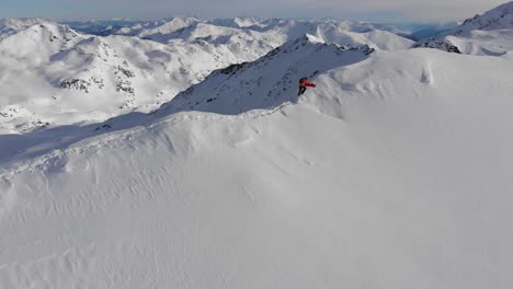 Beautiful-drone-shot-of-snowboarder-walking-on-thin-ridge-towards-the-summit