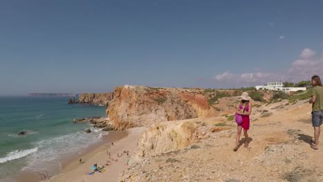 Right-to-left-pan-of-two-travellers-overlooking-Praia-do-Tonel,-Sagres-Portugal