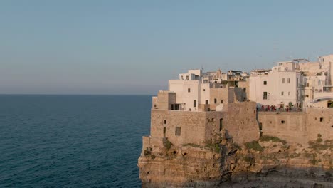 Beautiful-drone-aerial-shot-at-golden-hour-in-Polignano-a-Mare-showing-the-city-on-the-cliffs-with-the-sea-and-blue-sky,-Amazing-old-italian-city-at-sunset-in-the-region-of-Apulia-in-South-Italy
