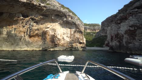 Approaching-a-protected-swimming-area-and-beach-on-shore-of-Hvar,-Croatia-with-steep-limestone-cliffs-and-small-inflatables