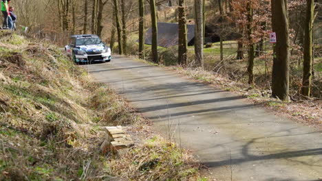 Passage-of-a-Skoda-Fabia-racing-car-during-a-Valasska-rally-among-trees-on-an-asphalt-road,-leaving-the-car-leaving-stones-and-leaves-as-they-pass-through-the-forest-captured-in-120fps-slow-motion