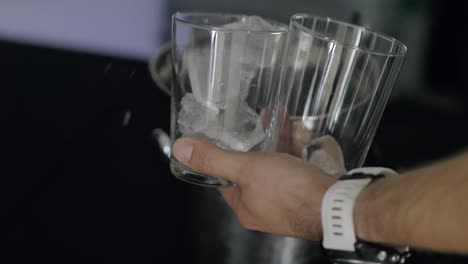Bartender-putting-ice-cubes-into-transparent-glasses-making-refreshing-beverages-close-up
