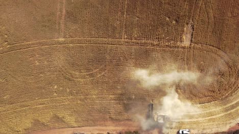 Straight-down-aerial-view-of-a-combine-harvesting-crops-and-spreading-dust-up-into-the-sky