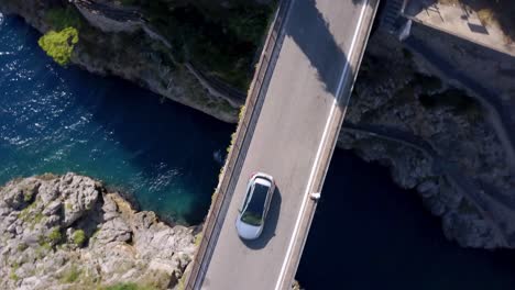 Fiordo-di-Furore-arch-bridge-in-Italy-with-car-traffic-and-a-man-crossing-the-stretch,-Aerial-drone-top-view-rotating-shot
