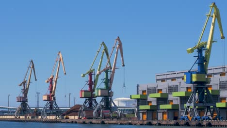 Port-cranes-and-harbor-warehouses-in-sunny-calm-summer-day-at-Port-of-Ventspils,-wide-shot-from-a-distance