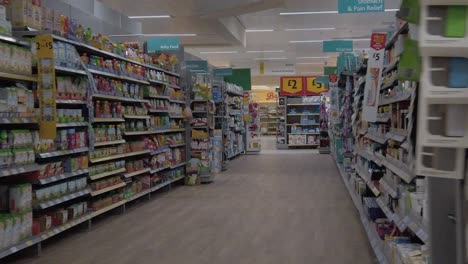 Slow-motion-interior-empty-UK-supermarket-dolly-left-passing-gift-cards-and-baby-food-aisle