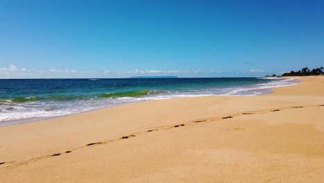 4K-Hawaii-Kauai-low-shot-trucking-in-on-beach-along-ocean-waves-coming-in-from-left-with-mostly-sunny-sky