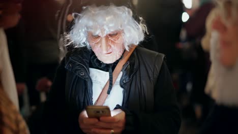 Person-with-Scary-horror-mask-outfit-on-halloween-event-writing-message-on-smartphone