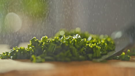 close-shot-of-fresh-chopped-chives-laying-on-a-wooden-cutting-board,-then-water-is-sprayed-on-it