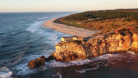 Lighthouse-in-Nazare-Portugal-near-Praia-do-Norte-during-sunset,-Aerial-circle-out-shot