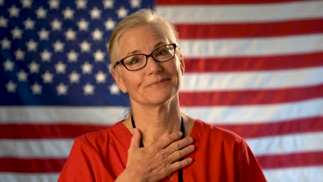 Mittelscharfes-Porträt-Einer-Krankenschwester,-Die-Glücklich-Und-Erleichtert-Aussieht,-Mit-Einer-Unscharfen-Amerikanischen-Flagge