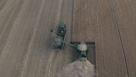 Top-down-aerial-follow-shot-of-full-combine-harvester-emptying-into-chaser-bin