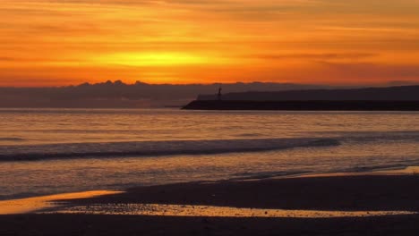 Orange-dawn-sky-over-sea-shore-with-harbor-wall