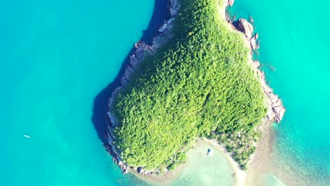Heart-shape-island-with-rocky-coastline-and-lush-vegetation-surrounded-by-calm-turquoise-lagoon-with-corals-in-Thailand