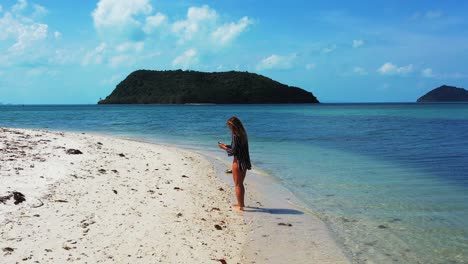 Attraktive-Junge-Frau,-Die-An-Einem-Wunderschönen-Exotischen-Strand-Spaziert,-Der-Von-Ruhigem,-Klarem,-Transparentem-Meerwasser-Umspült-Wird,-Und-Selfie-Fotos-In-Thailand-Macht
