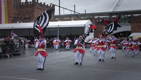 Gran-Grupo-De-Bailarines-En-El-Desfile-De-Carnaval-De-Aalst-Y-Al-Frente-Del-Grupo-De-Artistas-Ondeando-Grandes-Banderas