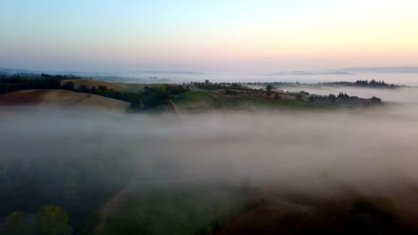 Sunrise-with-Tuscan-countryside-fields-in-Italy-on-a-cold-fog-filled-morning,-Aerial-left-pan-lowering-shot
