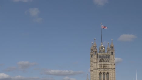 Bandera-Union-Jack-Sobrevolando-El-Palacio-De-La-Torre-Victoria-De-Westminster,-Londres,-Inglaterra-Contra-El-Cielo-Azul-Y-Las-Nubes