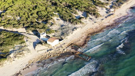 Trenc-Beach-in-Mallorca-Spain-with-small-restaurant-bar-near-a-reclaimed-building-structure-by-the-sea,-Aerial-flyover-view