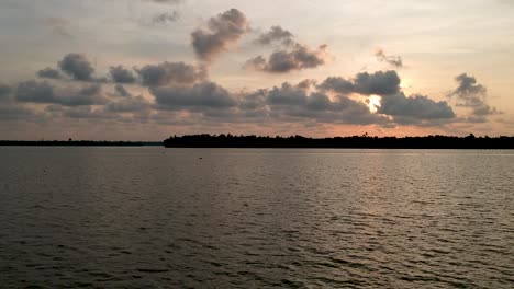 Beautiful-aerial-shot-of-a-backwater-Vembanadu-Lake-,-sunset,coconut-trees-,water-transportation,clouds,water-lines,twilight