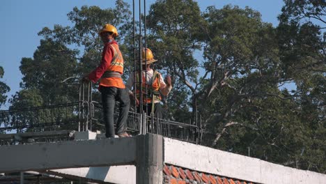 Wide-Exterior-Shot-of-Construction-Workers-on-the-Roof-of-a-Building-with-Hard-Hats-and-High-Visibility-Jackets