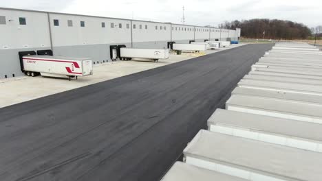 Tractor-trailer-trucks-lined-up-at-distribution-center-shipping-dock,-aerial-drone-footage-at-freight-and-logistics-warehouse