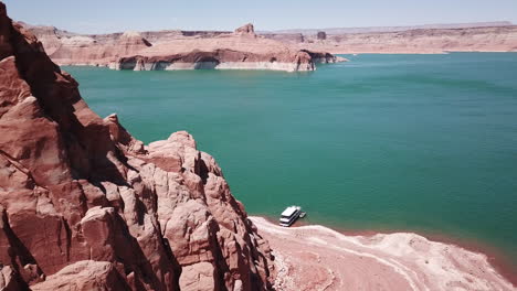 Drone-shot-flying-past-large-red-rocks-on-Lake-Powell-to-reveal-a-houseboat-and-the-lake