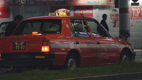 Taxi-Naranja-Que-Abre-La-Puerta-Para-Que-Los-Pasajeros-Suban-Y-Luego-Se-Van-A-La-Bahía-Por-La-Noche-En-Kamata,-Tokio,-Japón