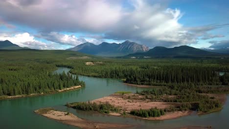Spectacular-countryside-scenic-flight-above-Yukon-Takhini-green-river-by-evergreen-tree-forest-and-Mount-Ingram-mountain-range-in-background-on-dramatic-blue-sunny-day,-Canada,-overhead-aerial