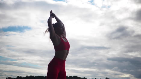 Young-woman-in-red-sportswear-doing-exercises-and-practicing-yoga-outside