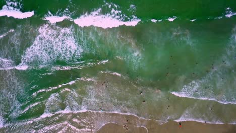 Aerial-top-down-shot-of-sea-waves-crashing-on-the-beach-and-people-on-the-water