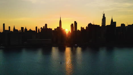 Silhouette-Eines-Wolkenkratzers,-Gleitendes-Luftfoto-Von-New-York-City-Zur-Goldenen-Stunde,-Wobei-Die-Sonne-Die-Stadt-Von-Einer-Seite-Zur-Anderen-Durchquert