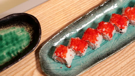 Delicious-Sushi-Rolls-In-A-Plate-Topped-With-Orange-Roe---high-angle-panning-shot,-slow-motion