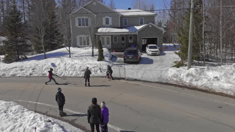 Kids-Play-Hockey-on-a-Street-in-Saint-Maurice-that-is-Covered-in-Snow-during-Winter,-Drone-Circle-Orbit-Aerial