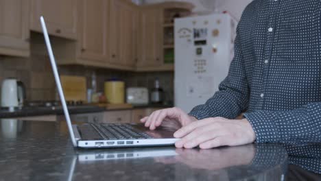 Smartly-dressed-man-using-the-track-pad-and-typing-on-a-laptop-on-a-kitchen-counter-while-working-from-home
