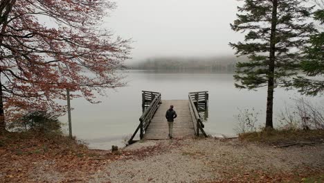 A-man-walking-away-from-the-camera-onto-a-wooden-pier-on-a-lake