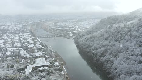 Snowfall-over-Kyoto,-Arashiyama-area-and-Togetsu-kyo-Bridge,-Aerial-View