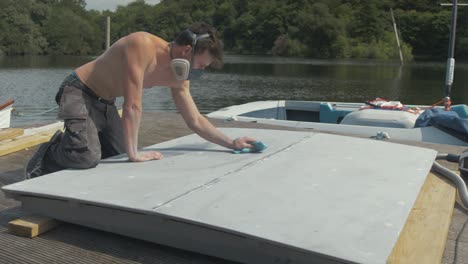 Young-shirtless-man-wiping-down-plywood-engine-cover-with-acetone-before-painting