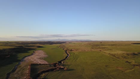 Aerial-view-of-green-rural-field-at-sunset-with-stream-going-through-it