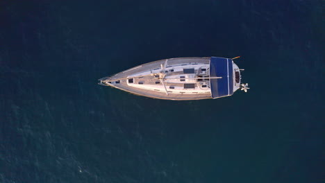 Overhead-4k-shot-of-a-luxurious-private-yacht-with-a-tall-mast-slowly-rocking-on-waves-of-a-dark-blue-sea-close-to-a-rocky-coast-on-a-sunny-summer-day