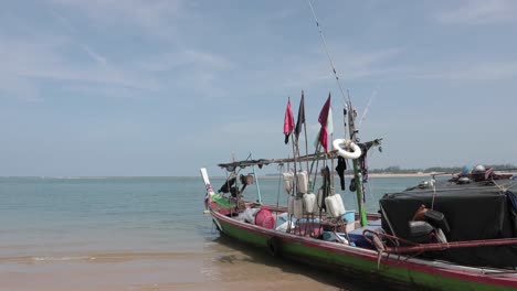 Fishing-boat-with-colorful-flags-on-a-beach-in-Thailand,-Takua-Pa-4K-Slow-Motion