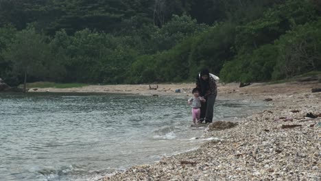 Islamist-woman-with-burka-and-little-kid-playing-on-shore-of-rocky-beach-in-Malaysia