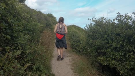 young-lady-hiking-along-the-cliffside-coastal-path-in-Torquay,-revealing-the-ocean-and-cliffs