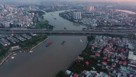 Aerial-slow-fly-in-over-the-Saigon-River-towards-Saigon-Bridge-with-cargo-boats-transporting-shipping-containers-to-the-port