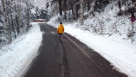Persona-Caminando-Por-Un-Camino-Forestal-En-Un-Bosque-De-Nieve-Invernal,-Seguimiento-Aéreo