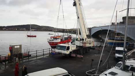 Hydraulic-crane-truck-lifting-heavy-fishing-boat-on-Conwy-Wales-harbour