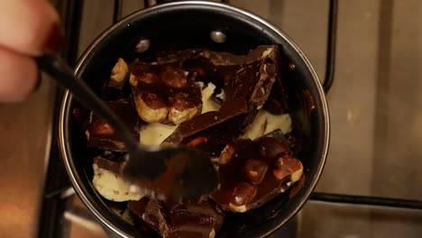 A-broken-milk-chocolate-bar-with-hazelnuts-mixed-with-butter-is-being-melted-on-the-gas-stove-while-a-female-with-a-marriage-ring-is-stirring-in-a-small-pot-for-melting