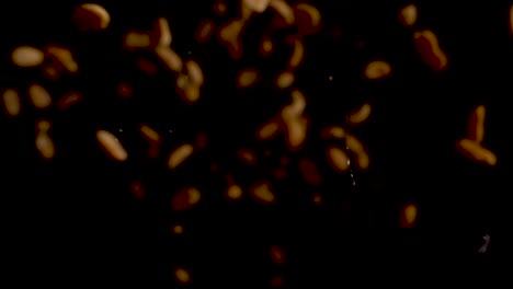 Many-illuminated-peanuts-falling-towards-lens-and-falling-down-on-black-surface