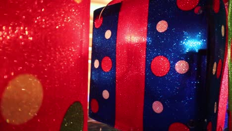 Vorbei-An-Bunt-Beleuchteten-Weihnachtsgeschenken,-Auf-Ein-Rot-blaues-Geschenk-Mit-Tupfen-Und-Roter-Schleife-Obenauf-Zu,-Das-Nach-Rechts-Versetzt-Positioniert-Ist