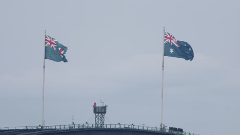 La-Bandera-Nacional-Australiana-Y-La-Bandera-Estatal-De-Nueva-Gales-Del-Sur-Vuelan-Sobre-El-Puente-Del-Puerto-De-Sydney-En-Sydney,-Australia---Primer-Plano,-Cámara-Lenta